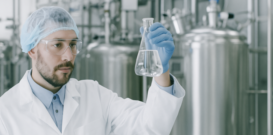 Scientist in GMP-compliant biologics facility holding a flask, with stainless steel bioreactors in the background and text reading “FDA GMP CDMO Biologics Europe.